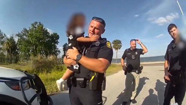 Tampa police officer carrying the child after saving the toddler's life. Tampa police officer carrying the child after saving the toddler's life.