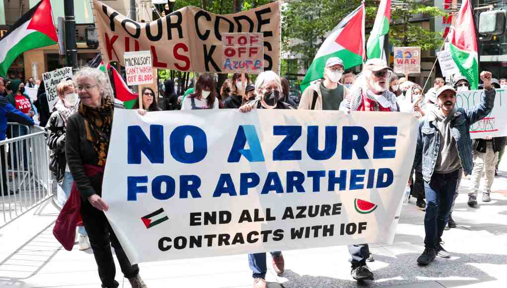Manifestación en la calle con pancartas que denuncian la colaboración de Microsoft Azure con fuerzas israelíes. Los participantes exigen el fin de los contratos tecnológicos relacionados, mostrando banderas palestinas y mensajes contra la guerra y el apartheid. Manifestación en la calle con pancartas que denuncian la colaboración de Microsoft Azure con fuerzas israelíes. Los participantes exigen el fin de los contratos tecnológicos relacionados, mostrando banderas palestinas y mensajes contra la guerra y el apartheid.