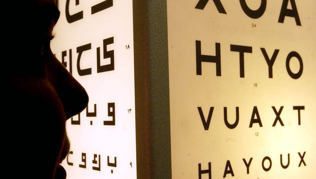 Persona observando de cerca un cartel luminoso de optometría con filas de letras en distintos tamaños, utilizado para pruebas de agudeza visual. Persona observando de cerca un cartel luminoso de optometría con filas de letras en distintos tamaños, utilizado para pruebas de agudeza visual.