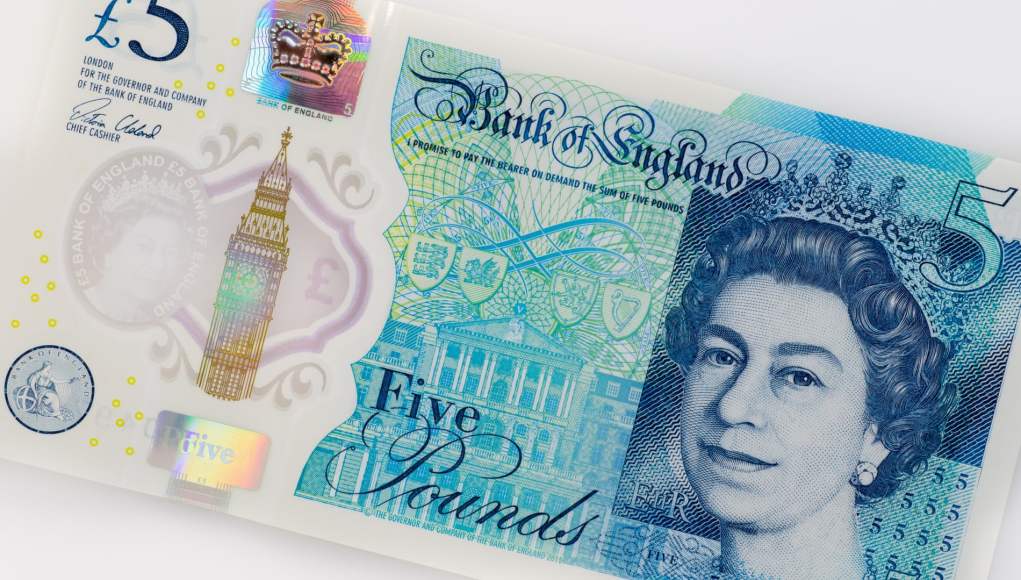 Primer plano de un billete de cinco libras esterlinas del Banco de Inglaterra. En el billete se muestra un retrato de la Reina Isabel II a la derecha, con detalles en tonos azules y verdes. A la izquierda, se ve una ilustración del Big Ben y varios elementos de seguridad, como un holograma y microimpresiones. En la parte superior izquierda se encuentra el símbolo de la libra esterlina (£) y el valor del billete (5). En el centro, el texto "Bank of England" y "Five Pounds". Primer plano de un billete de cinco libras esterlinas del Banco de Inglaterra. En el billete se muestra un retrato de la Reina Isabel II a la derecha, con detalles en tonos azules y verdes. A la izquierda, se ve una ilustración del Big Ben y varios elementos de seguridad, como un holograma y microimpresiones. En la parte superior izquierda se encuentra el símbolo de la libra esterlina (£) y el valor del billete (5). En el centro, el texto "Bank of England" y "Five Pounds".
