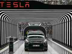 Las ventas de Tesla en Europa se desploman casi un 45% por los vínculos de Musk con Trump Automóvil Tesla negro saliendo de una línea de producción en una fábrica. El vehículo atraviesa un túnel iluminado con franjas LED blancas que crean un efecto visual futurista. Sobre la estructura del túnel, se ve el logotipo de Tesla en letras rojas. La matrícula del coche dice "GIGA 001", indicando su fabricación en la Gigafactory.