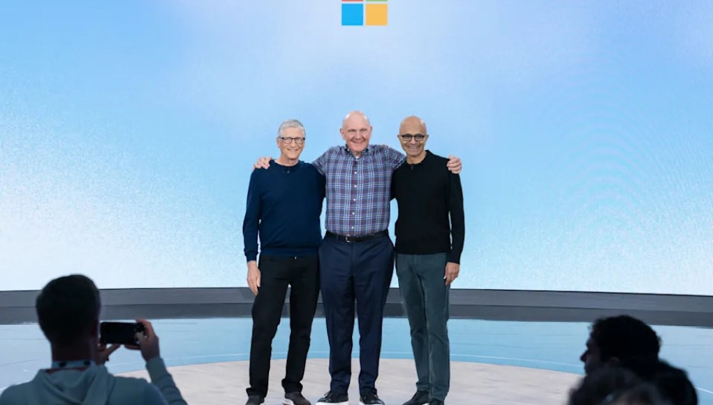Tres figuras destacadas del mundo tecnológico posan sonrientes en un escenario con el logotipo de Microsoft al fondo. Están abrazados, en un ambiente amistoso, mientras el público los fotografía. La imagen transmite un momento simbólico dentro de un evento importante de la compañía. Tres figuras destacadas del mundo tecnológico posan sonrientes en un escenario con el logotipo de Microsoft al fondo. Están abrazados, en un ambiente amistoso, mientras el público los fotografía. La imagen transmite un momento simbólico dentro de un evento importante de la compañía.