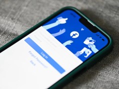 Meta multado con 102 millones dólares por almacenar contraseñas en texto plano Imagen de un teléfono móvil que muestra la pantalla de inicio de sesión de Facebook, con opciones para ingresar el número de teléfono o correo electrónico y la contraseña. El fondo de la pantalla incluye ilustraciones de manos interactuando con los iconos de "me gusta" y "compartir" de la red social. El dispositivo tiene un borde verde y está sobre una superficie gris.