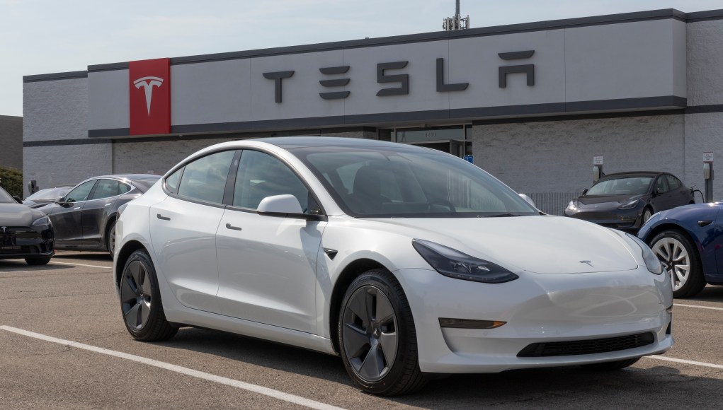 Tesla Model 3 blanco estacionado frente a una tienda de Tesla. La tienda tiene un cartel grande con el logo de Tesla y su nombre en la fachada. Otros vehículos Tesla están aparcados alrededor del Model 3, que está en primer plano y bien iluminado por la luz del día. Tesla Model 3 blanco estacionado frente a una tienda de Tesla. La tienda tiene un cartel grande con el logo de Tesla y su nombre en la fachada. Otros vehículos Tesla están aparcados alrededor del Model 3, que está en primer plano y bien iluminado por la luz del día.