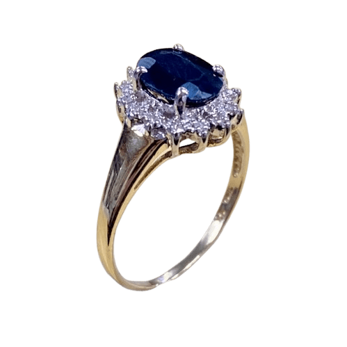 Ladies 9ct Yellow Gold 15 Stone Diamond & Sapphire Ring. Oval Sapphire In Rhodium 4 Claw Setting, Surrounded by 14 Single Cut Diamonds Illusion Bead Set in Rhodium Plated Basket, In Swept Up Shoulders. TDW 0.07ct. Size M/6.5, With Valuation Certificate – (NG 1307520)