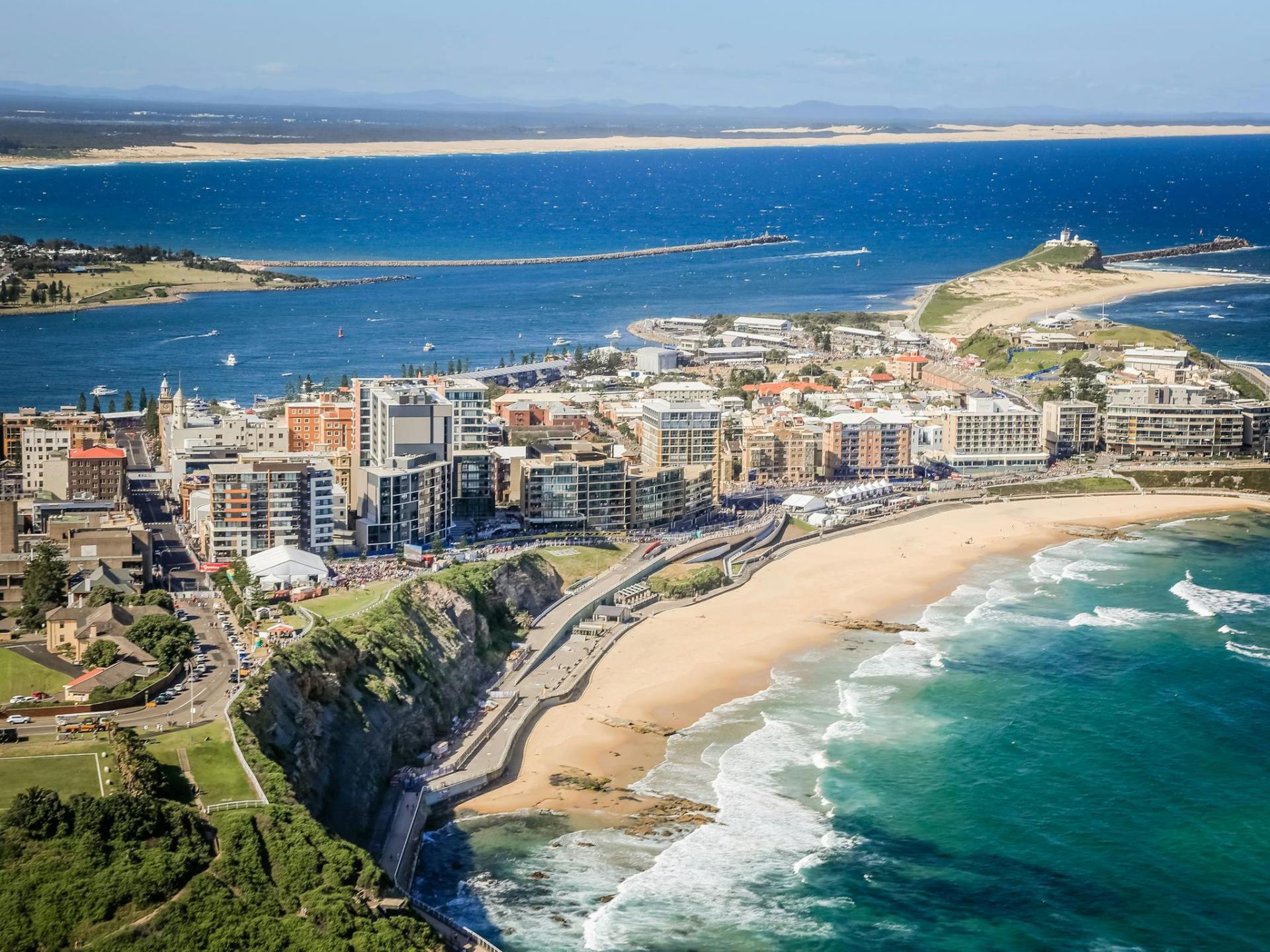 A scenic view of Newcastle Beach in Newcastle, showcasing sandy shores and gentle waves under a clear blue sky. A scenic view of Newcastle Beach in Newcastle, showcasing sandy shores and gentle waves under a clear blue sky.