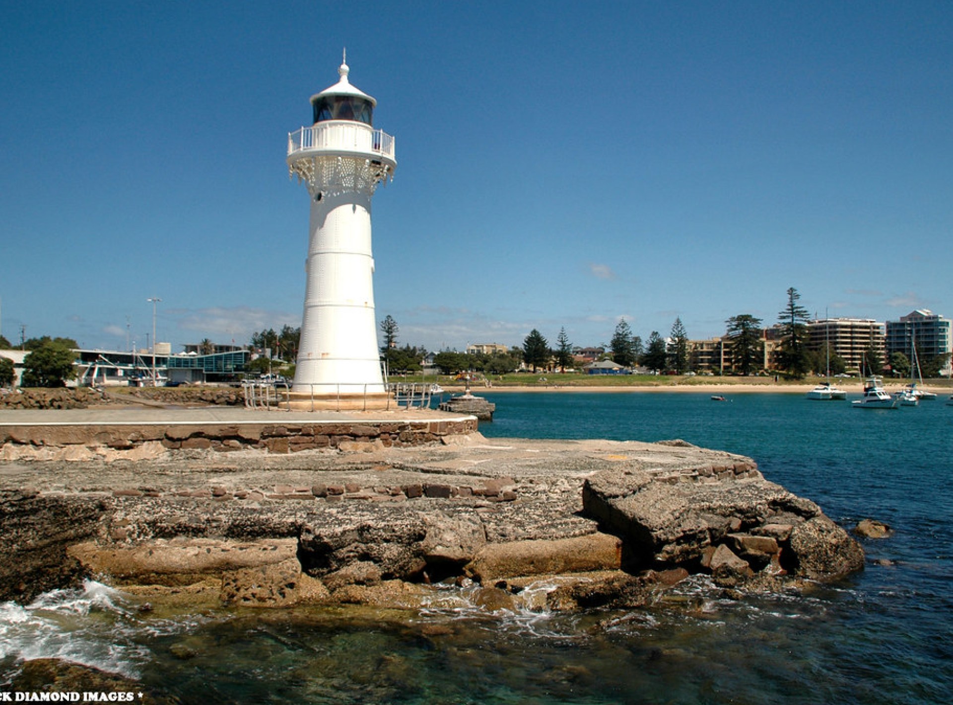 Lighthouse in Wollongong, Australia, standing tall against a blue sky with waves crashing on the rocks below. Lighthouse in Wollongong, Australia, standing tall against a blue sky with waves crashing on the rocks below.
