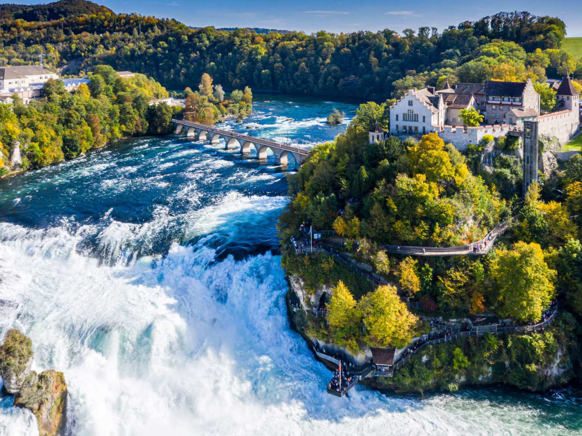 A stunning view of the Rhine Falls near Schaffhausen, showcasing cascading waters surrounded by lush greenery and rocky outcrops. A stunning view of the Rhine Falls near Schaffhausen, showcasing cascading waters surrounded by lush greenery and rocky outcrops.