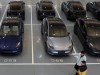 Tesla demanda a la UE por aranceles sobre vehículos eléctricos importados desde China Personas caminando en un estacionamiento cerrado con varios vehículos Tesla Model 3 en diferentes colores estacionados en filas, marcados con números de espacio como "065", "066" y "067". La escena muestra un ambiente organizado y limpio, con los autos eléctricos alineados de manera uniforme.