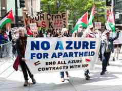 Microsoft investiga acusaciones de uso de su tecnología Azure por Israel para vigilancia masiva de palestinos Manifestación en la calle con pancartas que denuncian la colaboración de Microsoft Azure con fuerzas israelíes. Los participantes exigen el fin de los contratos tecnológicos relacionados, mostrando banderas palestinas y mensajes contra la guerra y el apartheid.