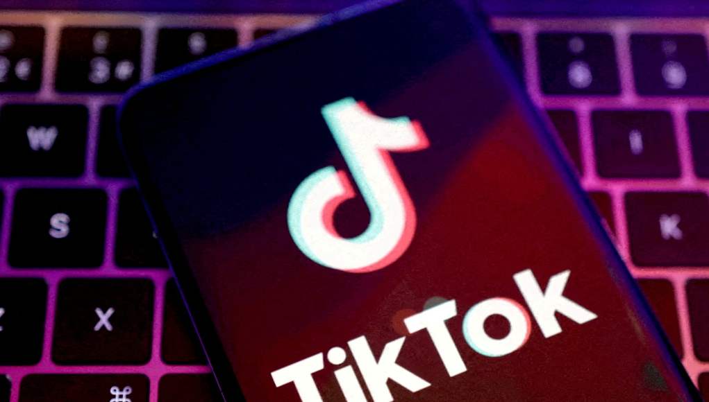 Teléfono móvil con la pantalla encendida mostrando el logotipo de TikTok, apoyado sobre un teclado retroiluminado de un ordenador portátil con luces de colores púrpura y rosa. Teléfono móvil con la pantalla encendida mostrando el logotipo de TikTok, apoyado sobre un teclado retroiluminado de un ordenador portátil con luces de colores púrpura y rosa.