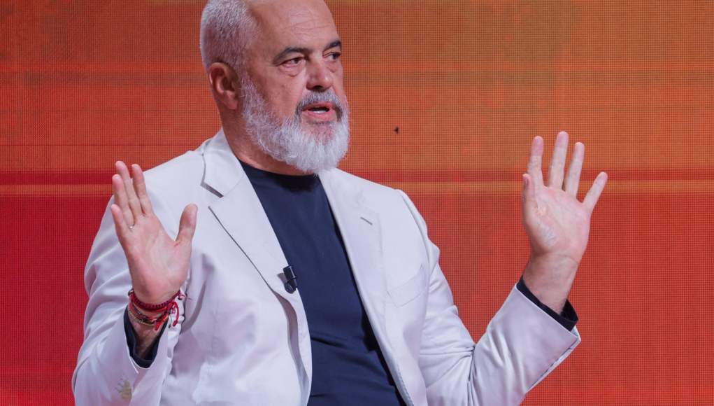 Hombre de cabello canoso y barba blanca, vestido con chaqueta clara y camiseta oscura, sentado frente a un fondo rojo anaranjado. Tiene ambas manos levantadas a la altura del pecho en un gesto expresivo mientras habla. Hombre de cabello canoso y barba blanca, vestido con chaqueta clara y camiseta oscura, sentado frente a un fondo rojo anaranjado. Tiene ambas manos levantadas a la altura del pecho en un gesto expresivo mientras habla.