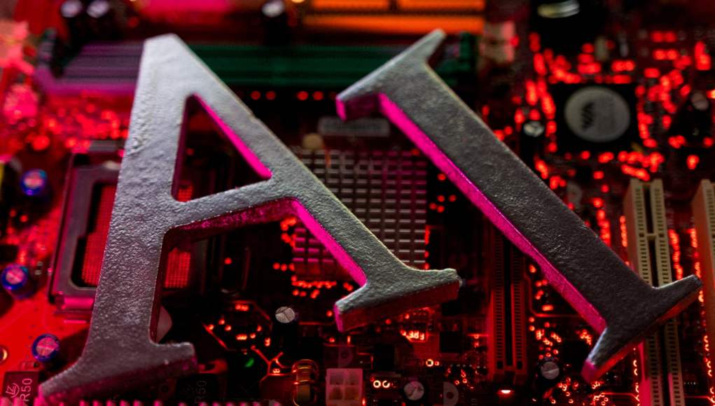 La palabra 'AI' en letras metálicas sobre un fondo de una placa base iluminada con luces rojas y rosadas, representando tecnología e inteligencia artificial. La palabra 'AI' en letras metálicas sobre un fondo de una placa base iluminada con luces rojas y rosadas, representando tecnología e inteligencia artificial.