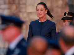 México demanda a Google por cambiar el nombre del Golfo de México para usuarios estadounidenses Mujer con expresión seria y vestimenta formal oscura durante un acto oficial, rodeada por personal militar desenfocado en primer plano.