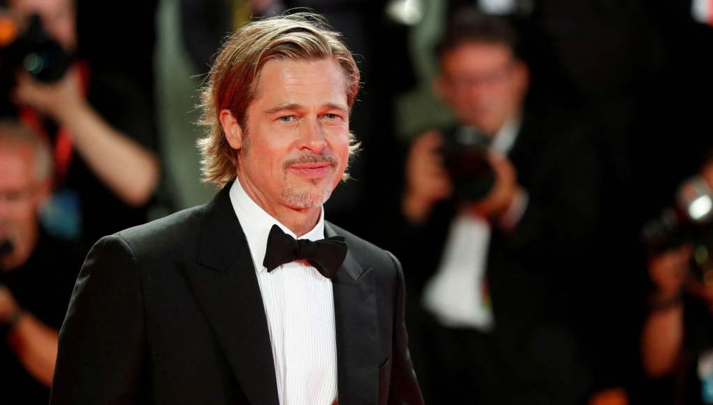 Un hombre sonriente vestido con un esmoquin negro y pajarita, con cabello rubio peinado hacia atrás y barba recortada, posando en lo que parece ser un evento formal con fotógrafos y cámaras desenfocados en el fondo. Un hombre sonriente vestido con un esmoquin negro y pajarita, con cabello rubio peinado hacia atrás y barba recortada, posando en lo que parece ser un evento formal con fotógrafos y cámaras desenfocados en el fondo.