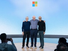 Microsoft posiciona la computación cuántica como próximo acelerador de la nube Tres figuras destacadas del mundo tecnológico posan sonrientes en un escenario con el logotipo de Microsoft al fondo. Están abrazados, en un ambiente amistoso, mientras el público los fotografía. La imagen transmite un momento simbólico dentro de un evento importante de la compañía.