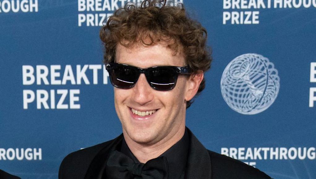 Hombre con esmoquin negro y gafas de sol sonríe frente a un fondo con el texto 'Breakthrough Prize' repetido. Hombre con esmoquin negro y gafas de sol sonríe frente a un fondo con el texto 'Breakthrough Prize' repetido.