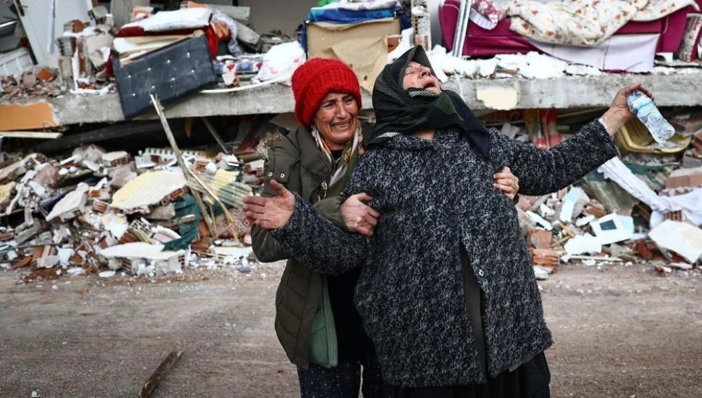 Mujeres llorando frente a los escombros de un edificio colapsado tras un desastre, expresando dolor y desesperación. Mujeres llorando frente a los escombros de un edificio colapsado tras un desastre, expresando dolor y desesperación.