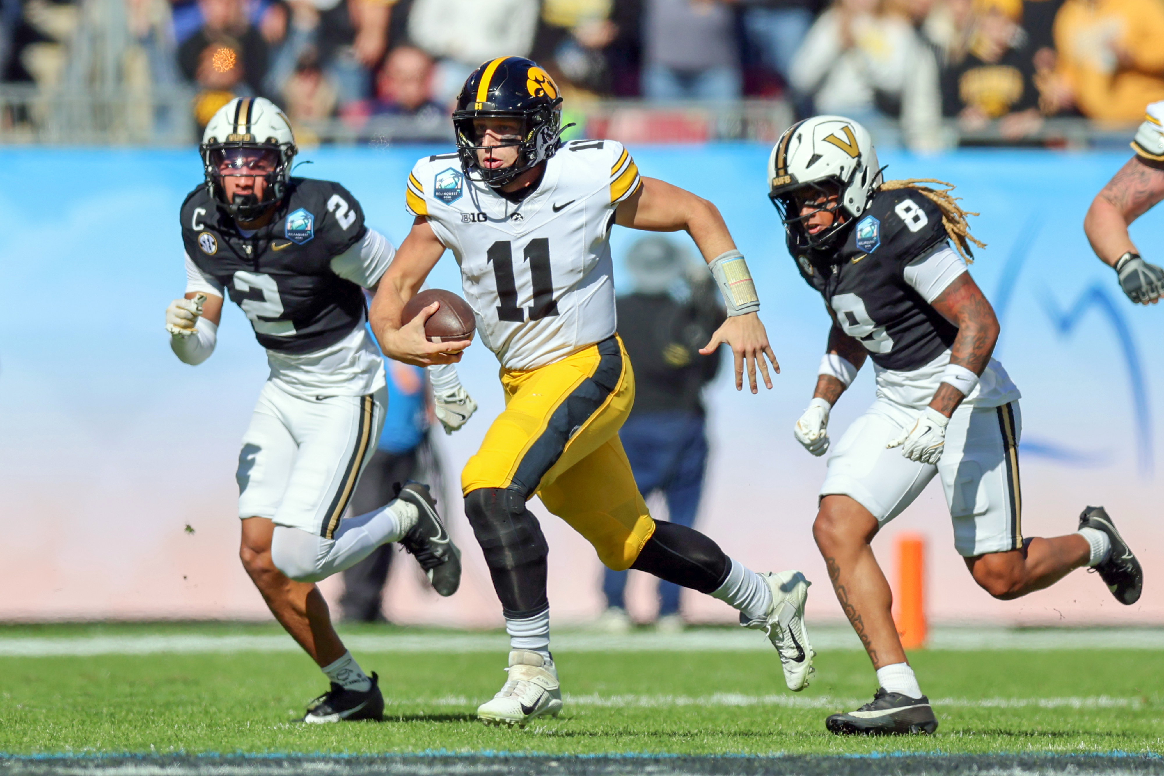 TAMPA, FLORIDA - DECEMBER 31: Mark Gronowski #11 of the Iowa Hawkeyes runs past Randon Fontenette #2 and CJ Heard #8 of the Vanderbilt Commodores during the first half of the ReliaQuest Bowl at Raymond James Stadium on December 31, 2025 in Tampa, Florida. (Photo by Mike Carlson/Getty Images)