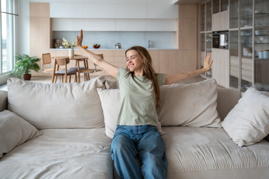 femeie frumoasă care stă pe canapea cu mâinile întinse pe un fundal deschis la culoare femeie frumoasă care stă pe canapea cu mâinile întinse pe un fundal deschis la culoare