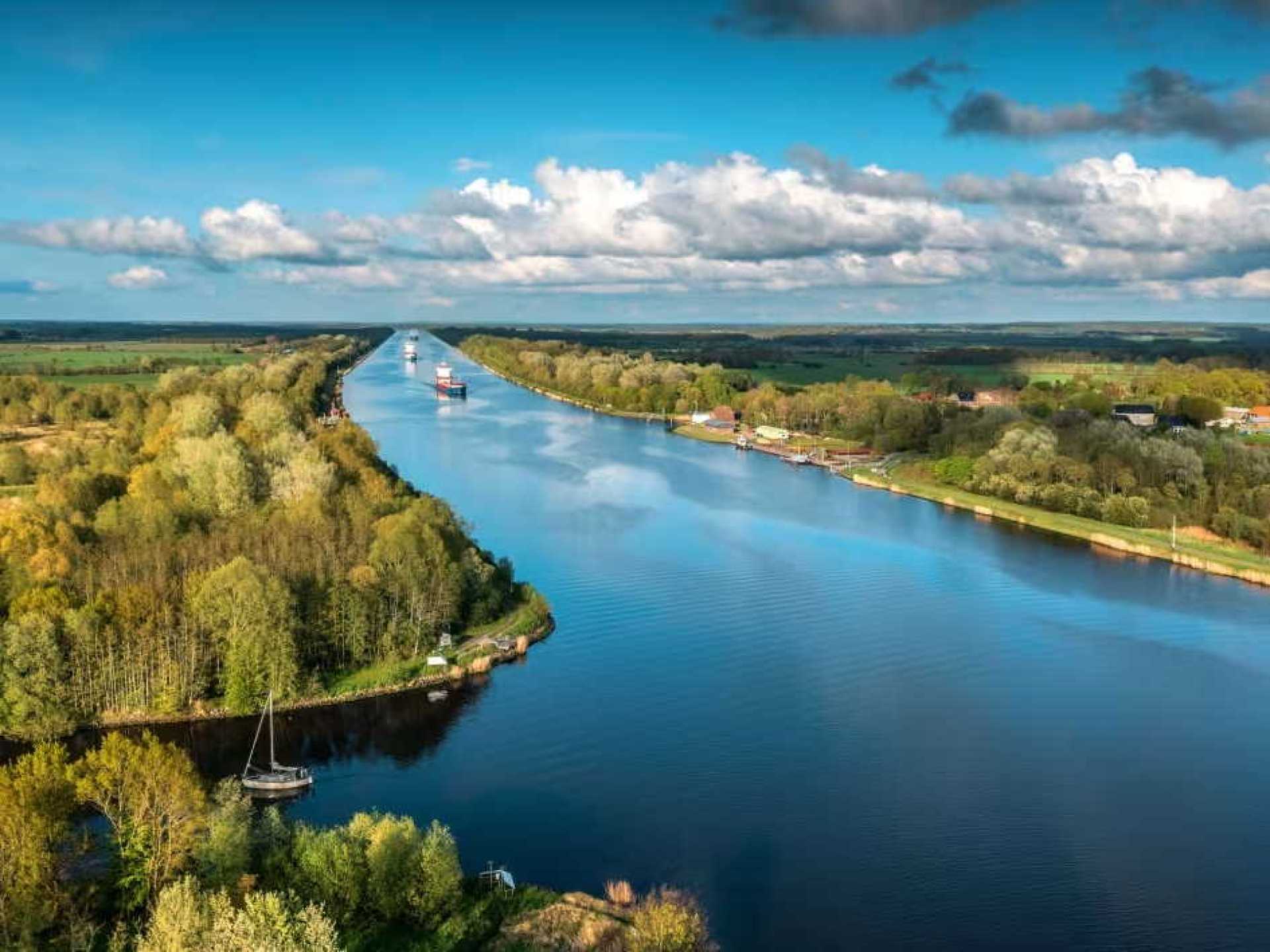 A scenic view of the Kiel Canal in Kiel, showcasing boats navigating through the waterway surrounded by lush greenery. A scenic view of the Kiel Canal in Kiel, showcasing boats navigating through the waterway surrounded by lush greenery.