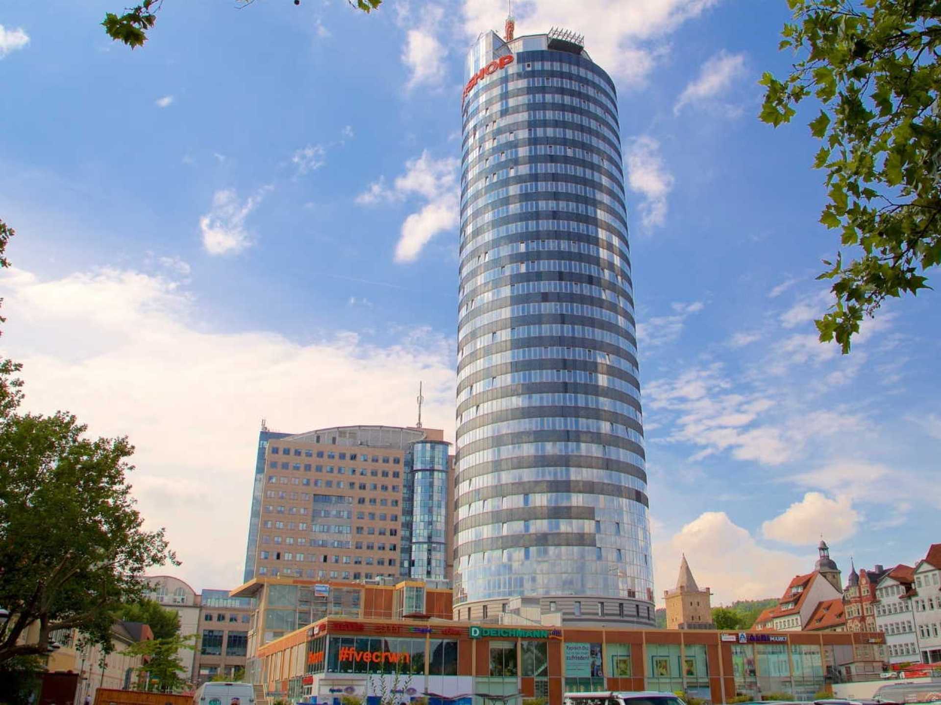 Alt text for the image: Scenic view of the Jen Tower in Jena, showcasing the city's skyline and lush greenery. Alt text for the image: Scenic view of the Jen Tower in Jena, showcasing the city's skyline and lush greenery.