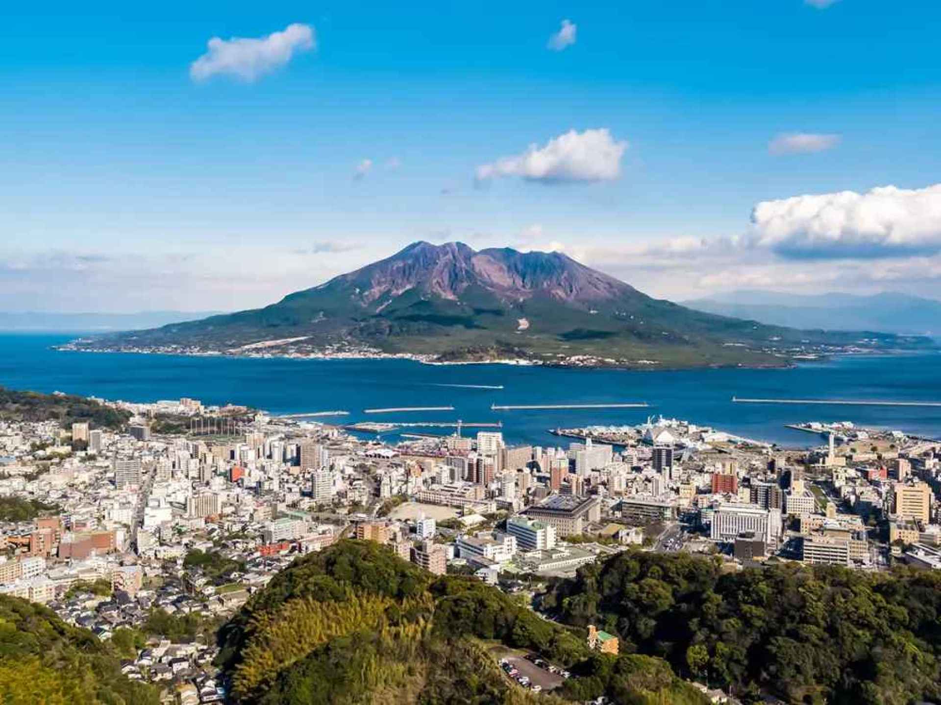 A scenic view of Sakurajima volcano surrounded by lush greenery and the tranquil waters of Kagoshima Bay. A scenic view of Sakurajima volcano surrounded by lush greenery and the tranquil waters of Kagoshima Bay.