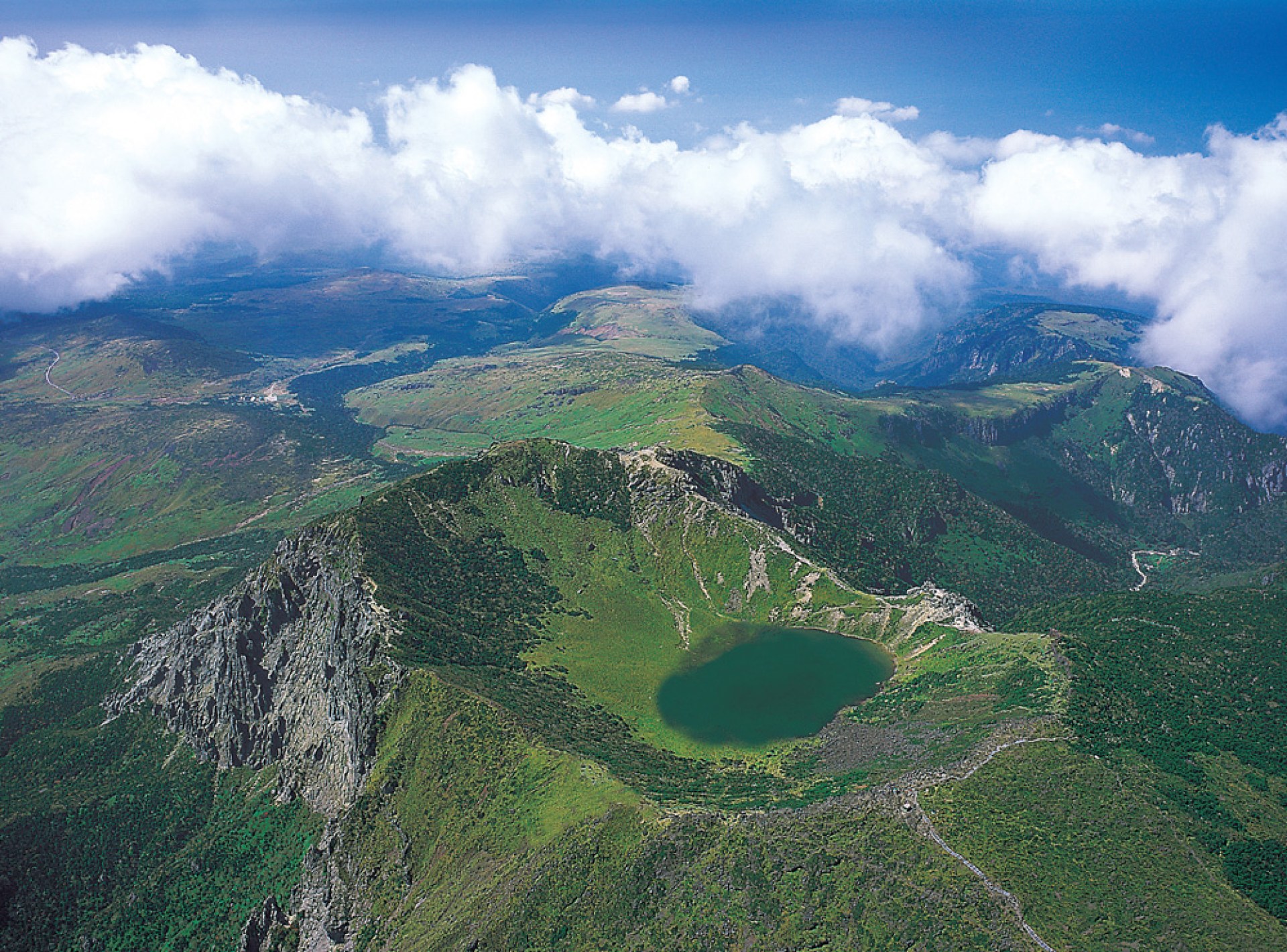 Scenic view of Hallasan Mountain in Jeju City, showcasing its lush greenery and dramatic peaks under a clear blue sky. Scenic view of Hallasan Mountain in Jeju City, showcasing its lush greenery and dramatic peaks under a clear blue sky.
